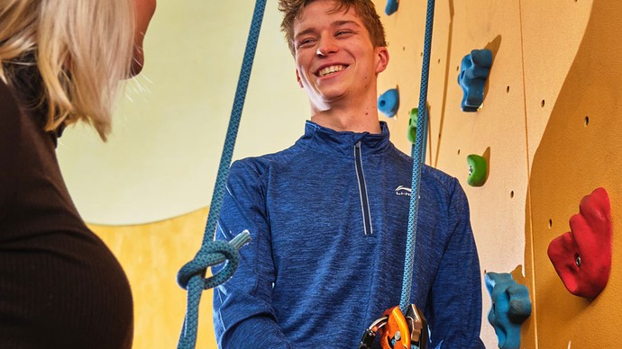 Junger lächelnder Mann mit Klettergurt vor einer Kletterwand