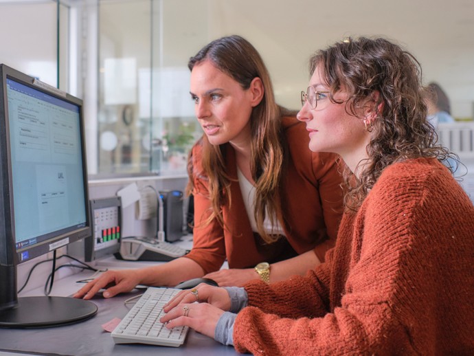 Zwei Frauen blicken auf einen Computer-Bildschirm.